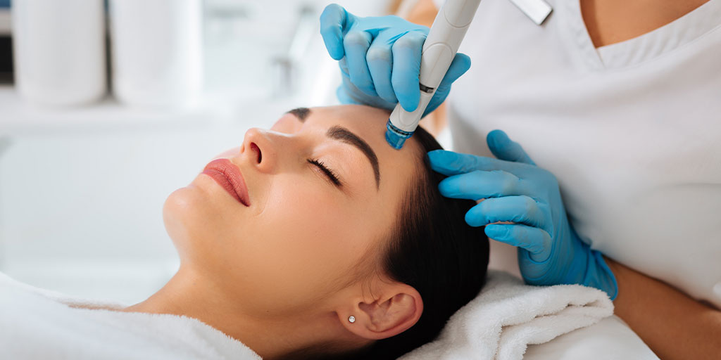 Woman laying on her back and receiving a facial treatment from a professional in blue gloves.