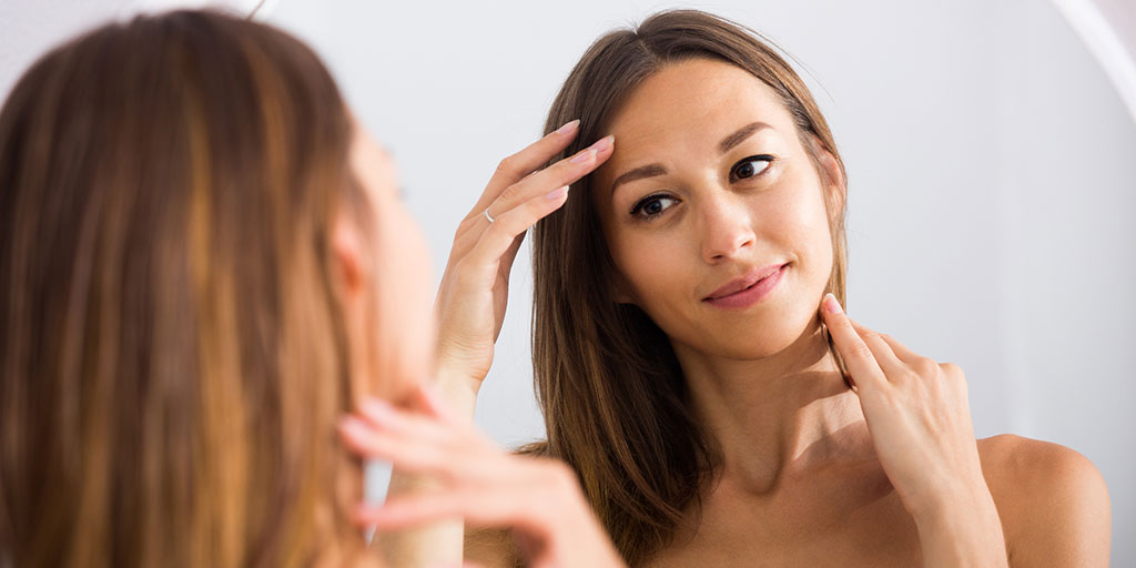 woman looking at skin in the mirror