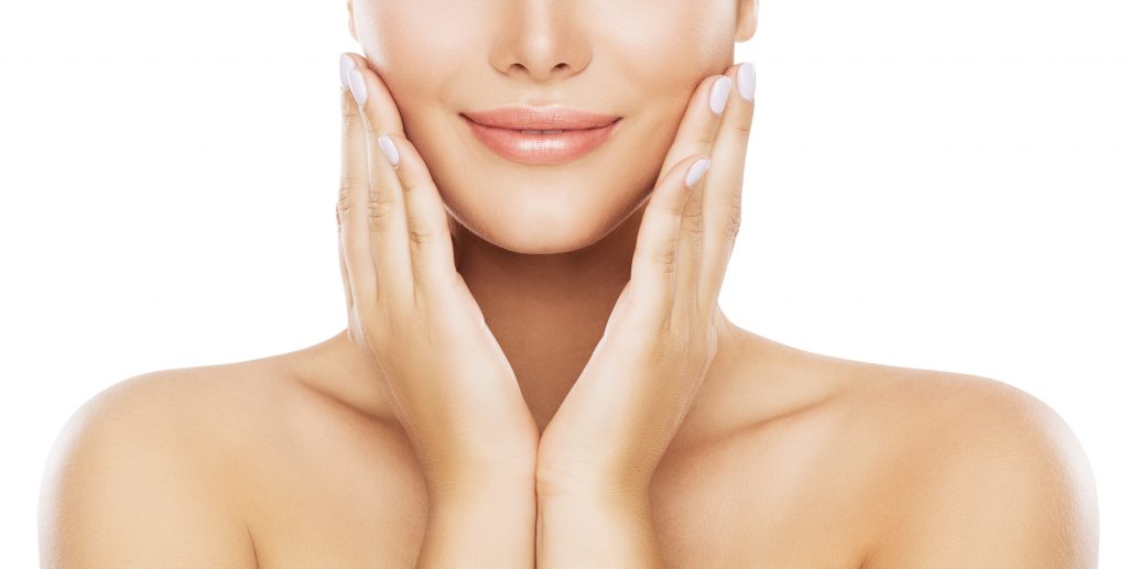 A woman with a bare upper body gently touching her cheeks, smiling softly.