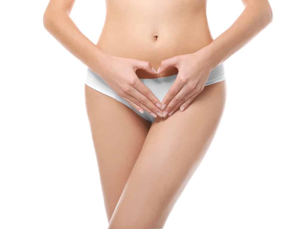 Woman in white underwear forms a heart shape with her hands over her lower abdomen.