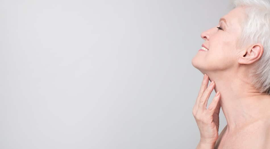Side profile of a woman touching her neck and jawline, against a plain light background.
