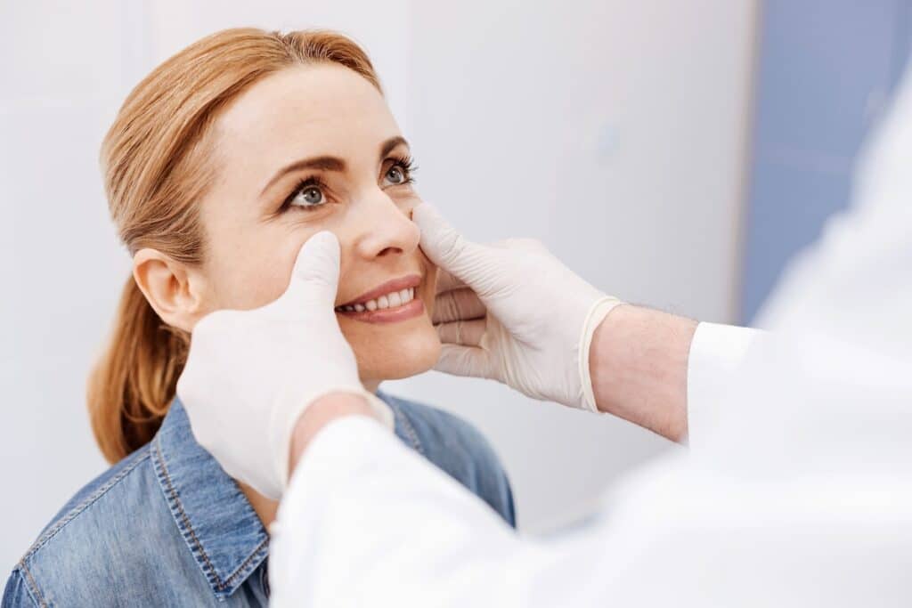 Woman smiling as a gloved professional places hands on her face.