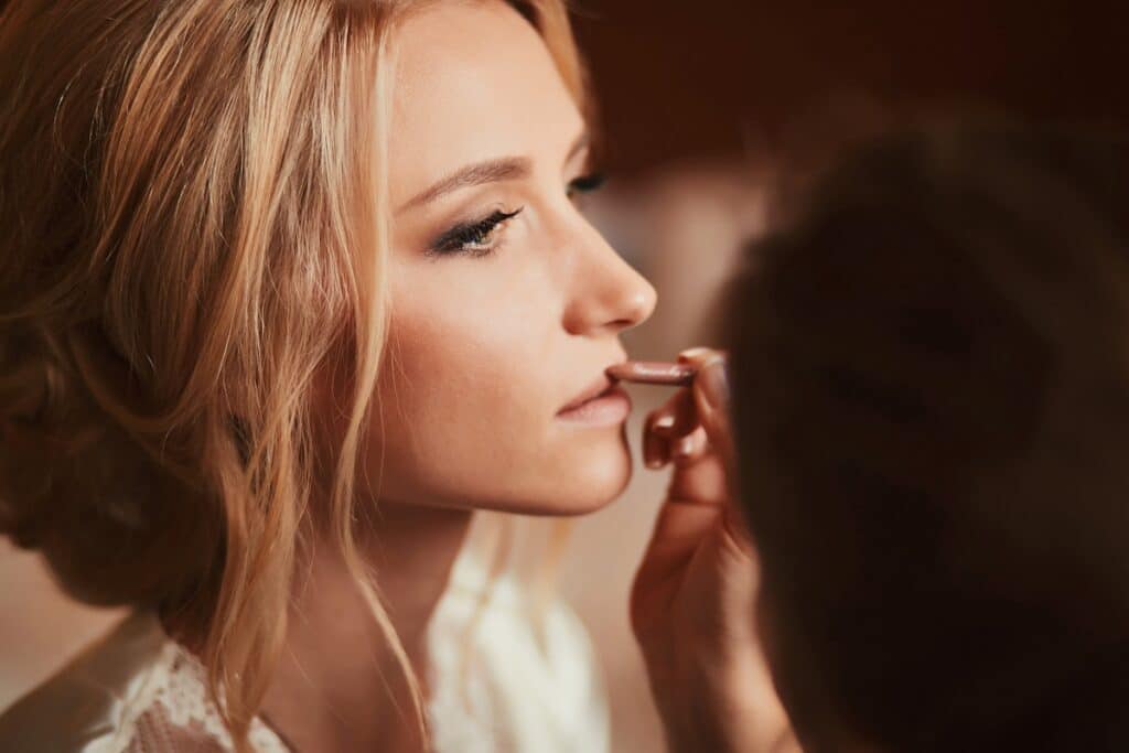 Close-up side view of a woman having lipstick applied by a makeup artist.