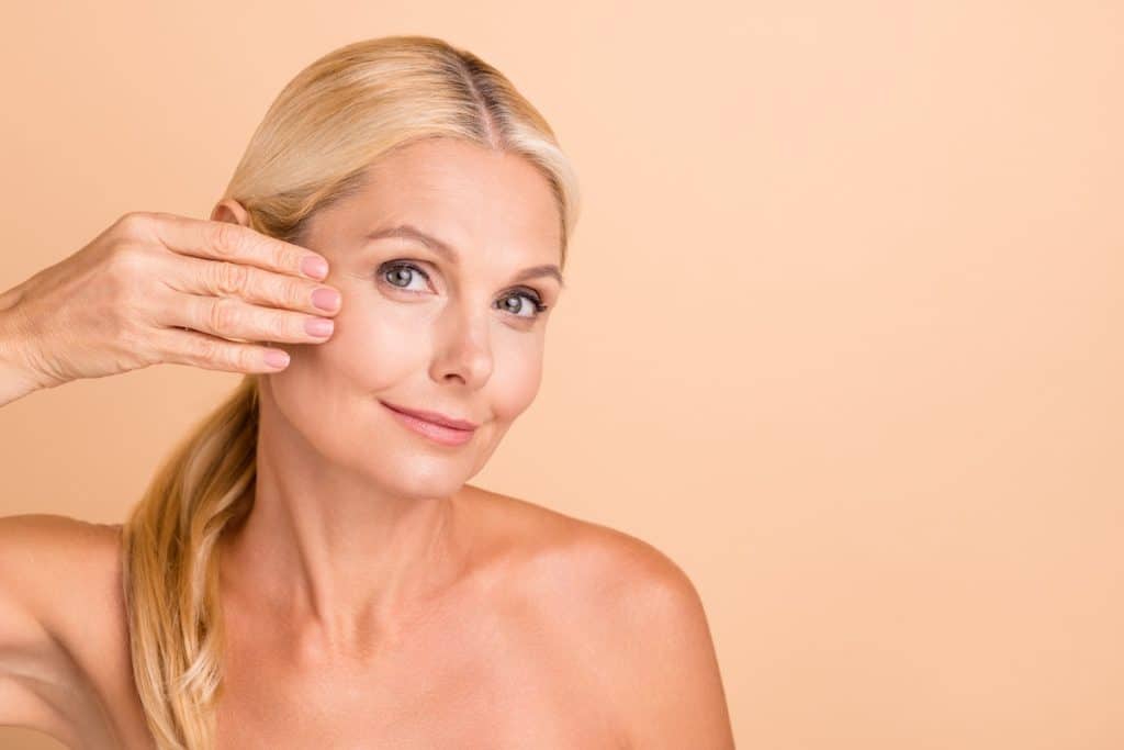 Confident middle-aged woman touching her face, symbolizing facelift results and rejuvenation.