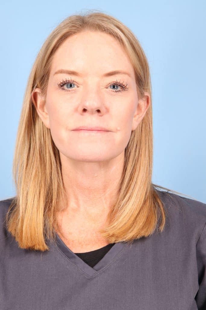 A woman with straight blonde hair and a neutral expression wearing a dark gray top, posed against a light blue background.